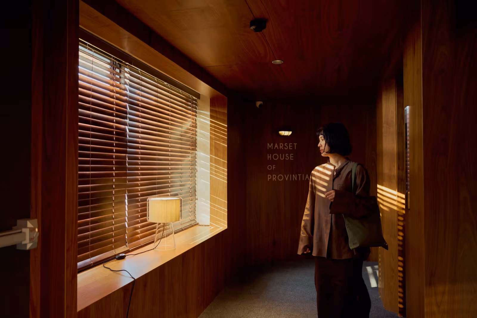 แสงลอดมู่ลี่เข้าสู่ทางเดินผนังไม้ที่มีข้อความ MARSET HOUSE OF PROVINTIA