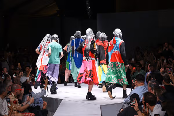 鮮やかなグラフィック服で一緒にランウェイを進むモデルたち