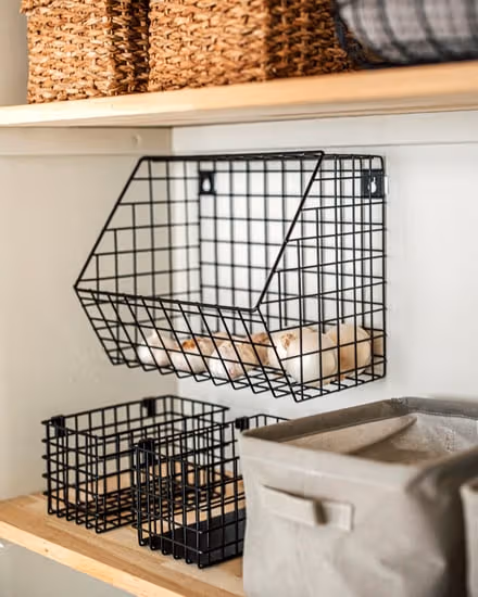 Black wire baskets and pale fabric boxes on wooden shelves