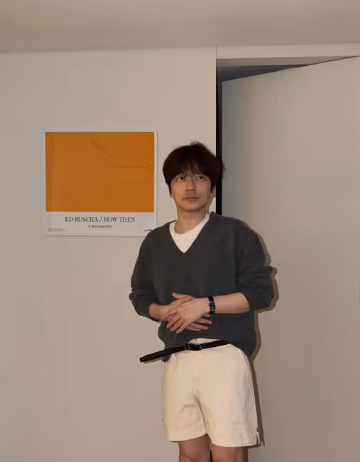Lee Dong-hwi adjusts a collegiate look with a charcoal V-neck and beige shorts.