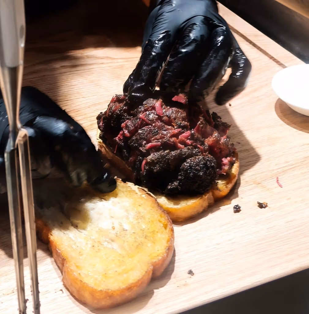 切ったパンへ塩漬け肉を載せる作業者