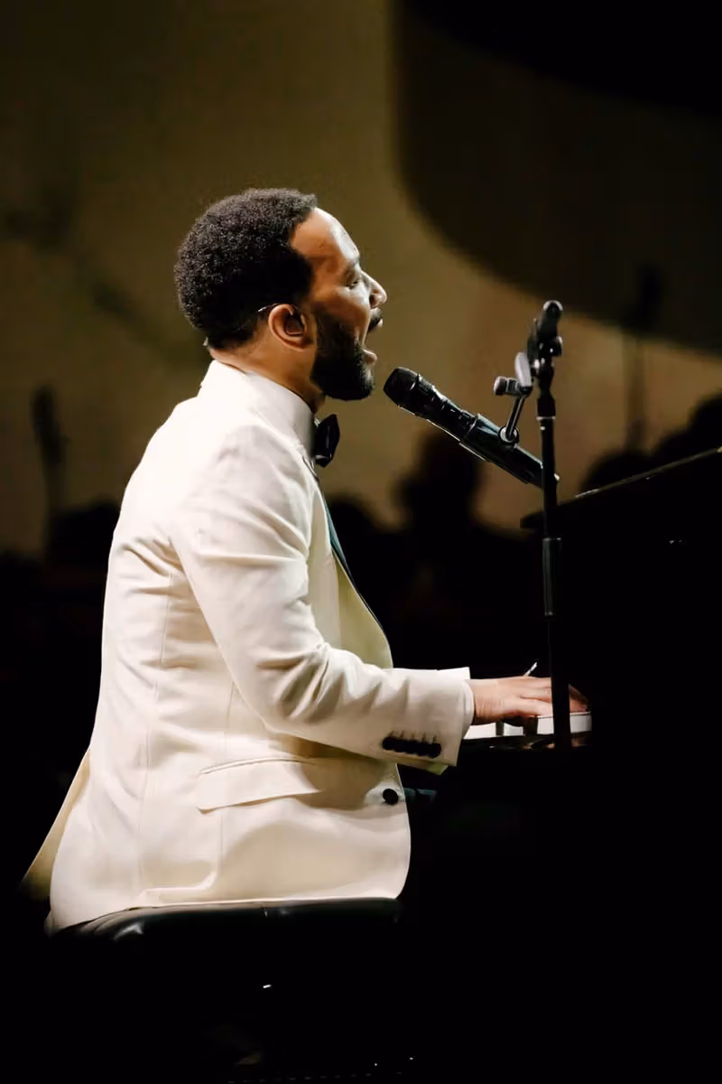 白いタキシードジャケットでピアノの前で歌うJohn Legend