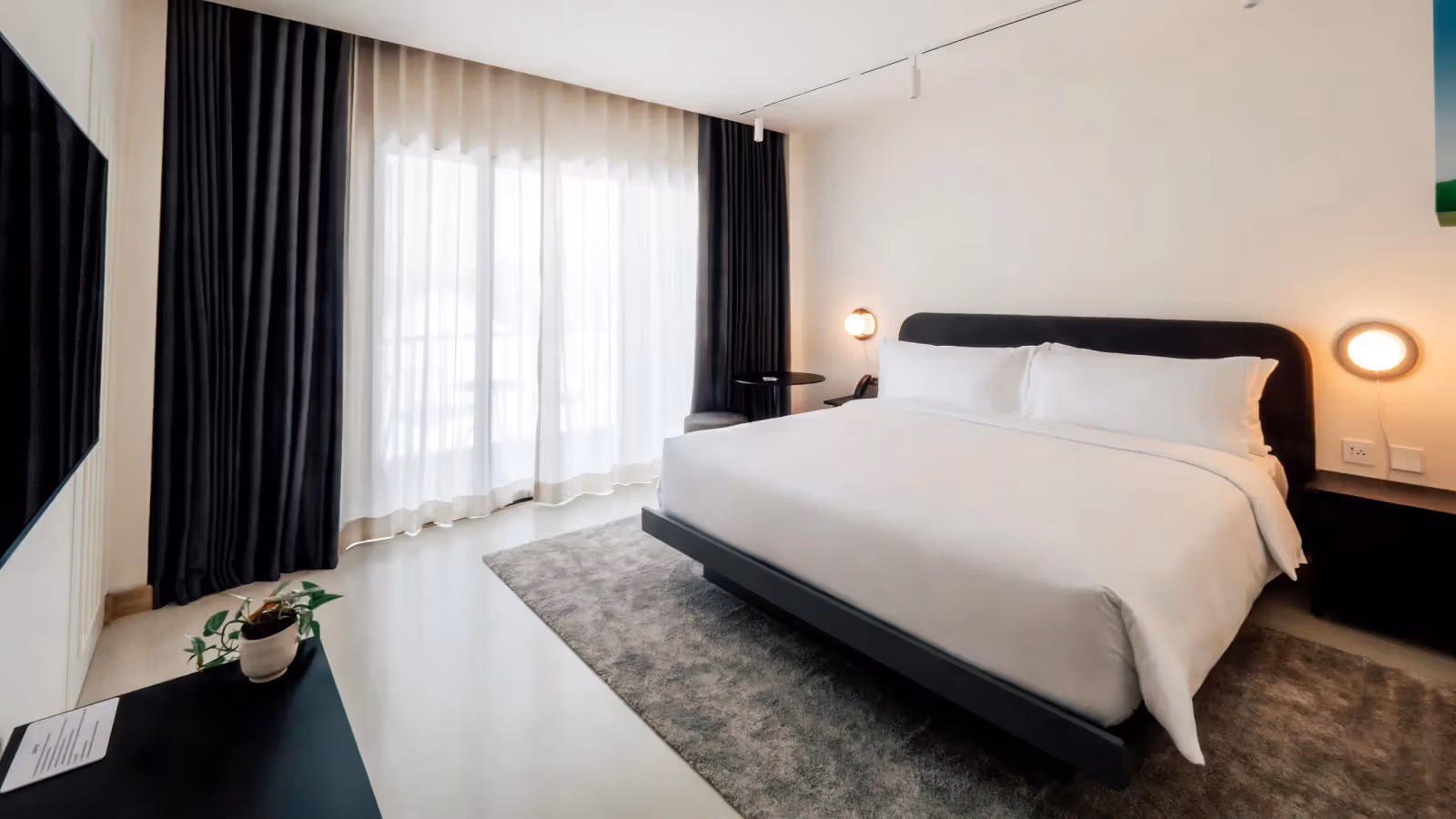 Guestroom with a white king bed, dark headboard and curtains, and two round wall lights