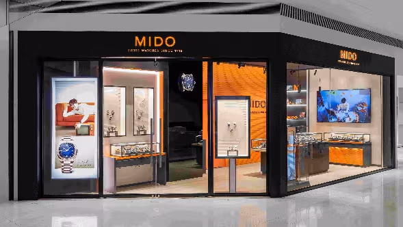 店面以黑色框架与玻璃界定入口，让橘色背墙与腕表展示向商场展开。