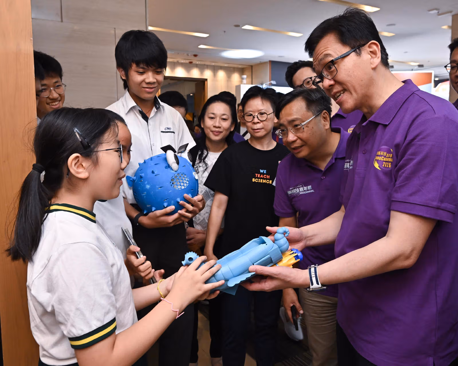 Students presenting blue models to guests wearing purple event shirts