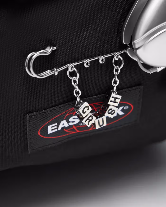 C, R, U, S and H letter charms hang below a long safety pin, with the bag’s original Eastpak label behind them.