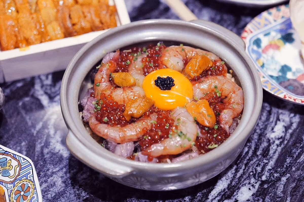 솥에 담은 식초 양념 밥 위에 성게알, 새우, 연어알, 달걀노른자를 올린다.