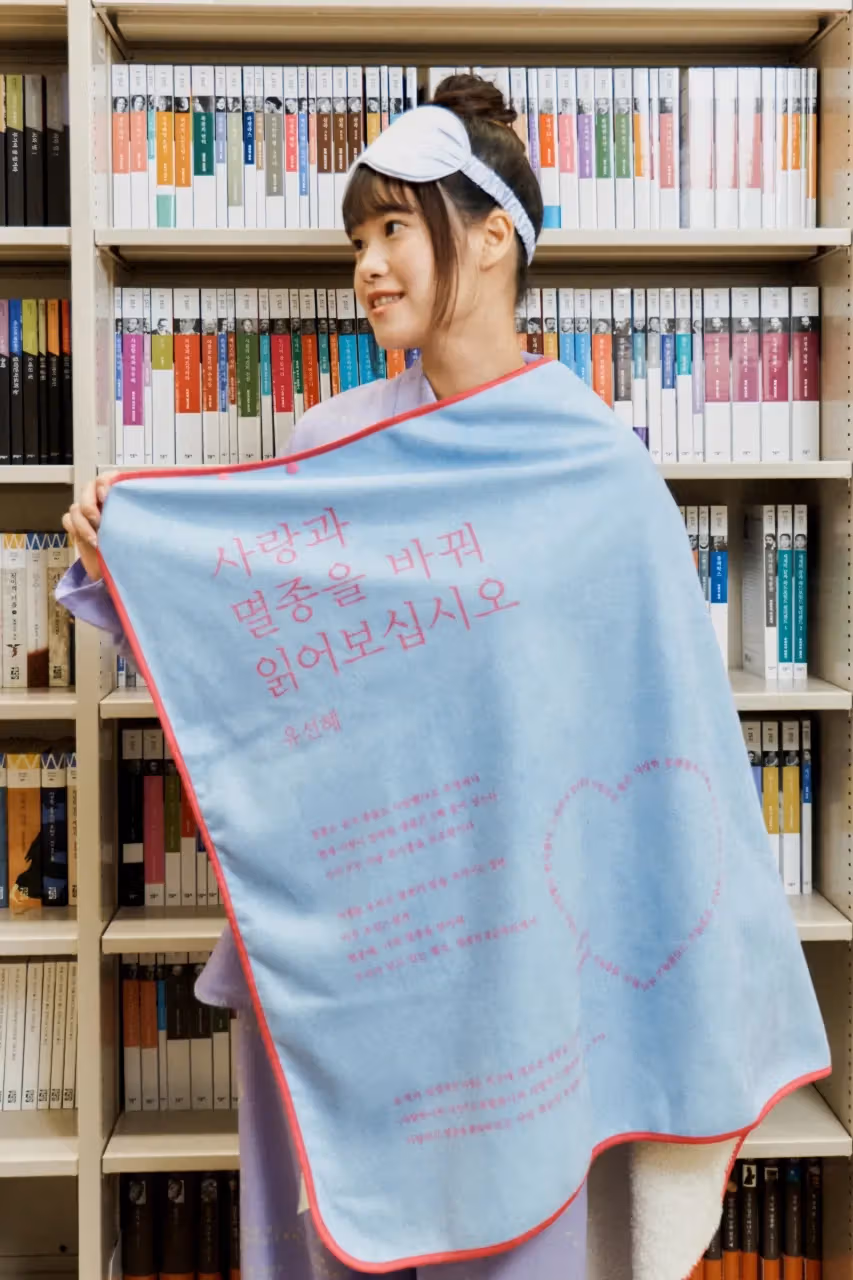 책장 앞에서 파란색 분홍 문자 담요를 펼친 인물