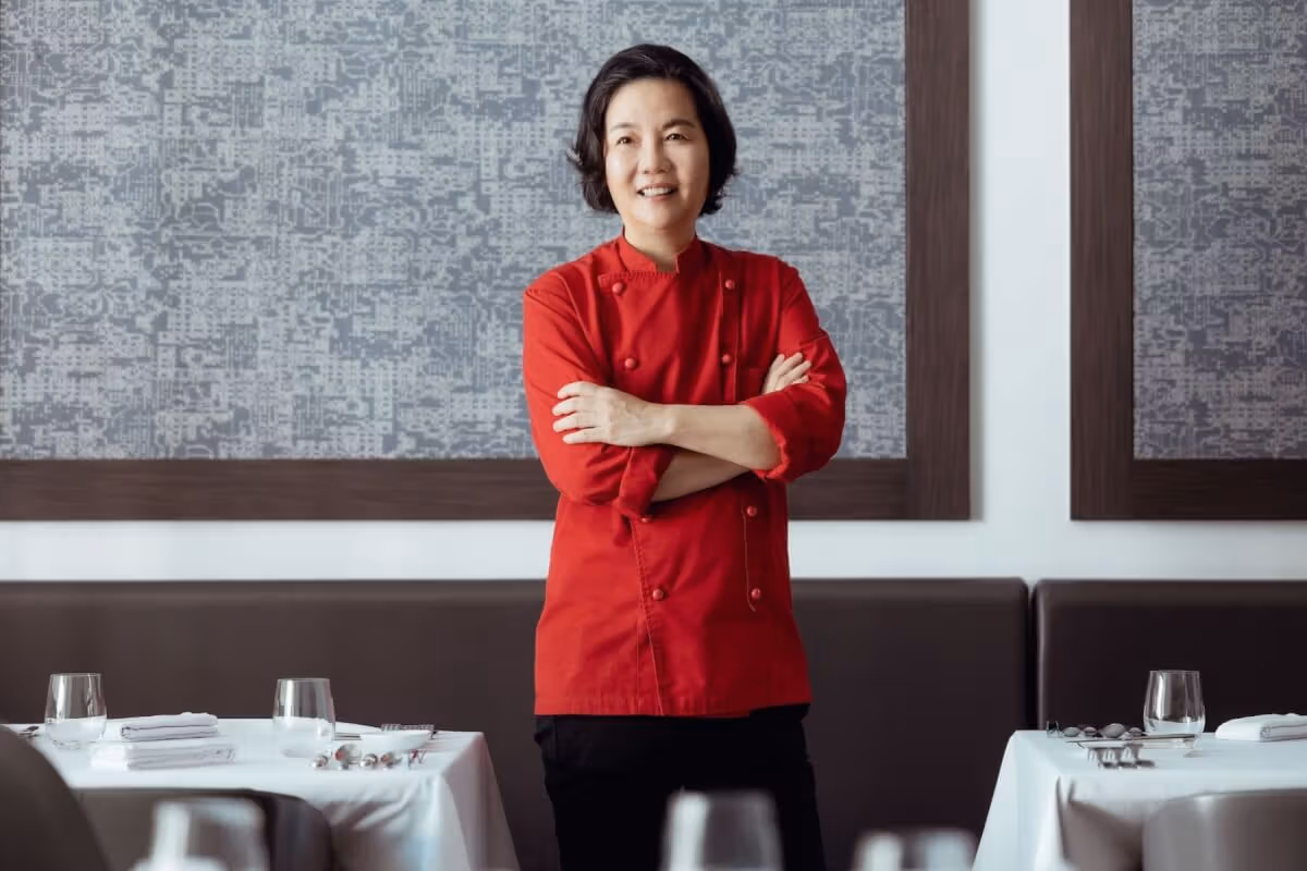 Justine Li in a red chef jacket beside white-clothed dining tables