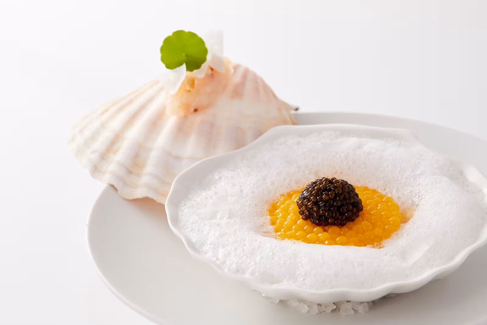 White flower-shaped plate with foam, orange-yellow pearls and dark caviar