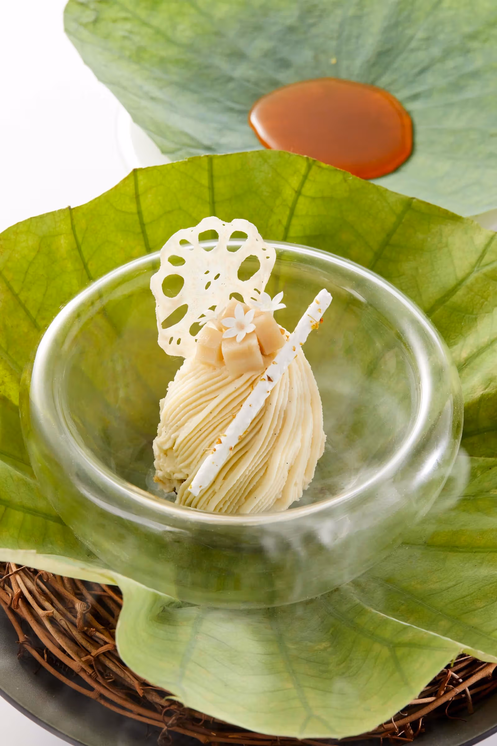 Finely piped dessert in a glass bowl with a thin lotus-root slice and green leaves
