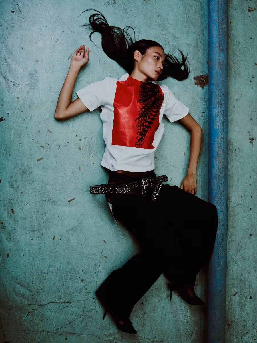Model in a red-and-black graphic white tee and black trousers against a green wall
