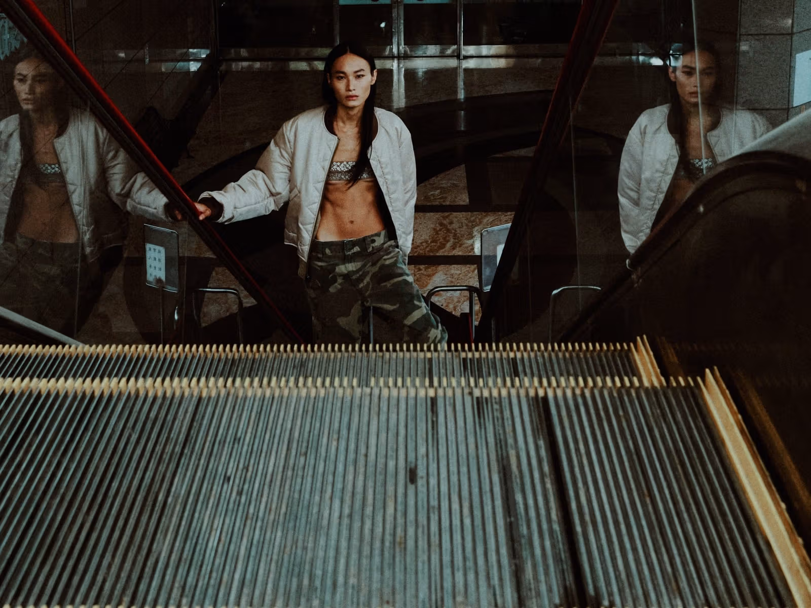Model in a light jacket and camouflage bottoms standing on an escalator