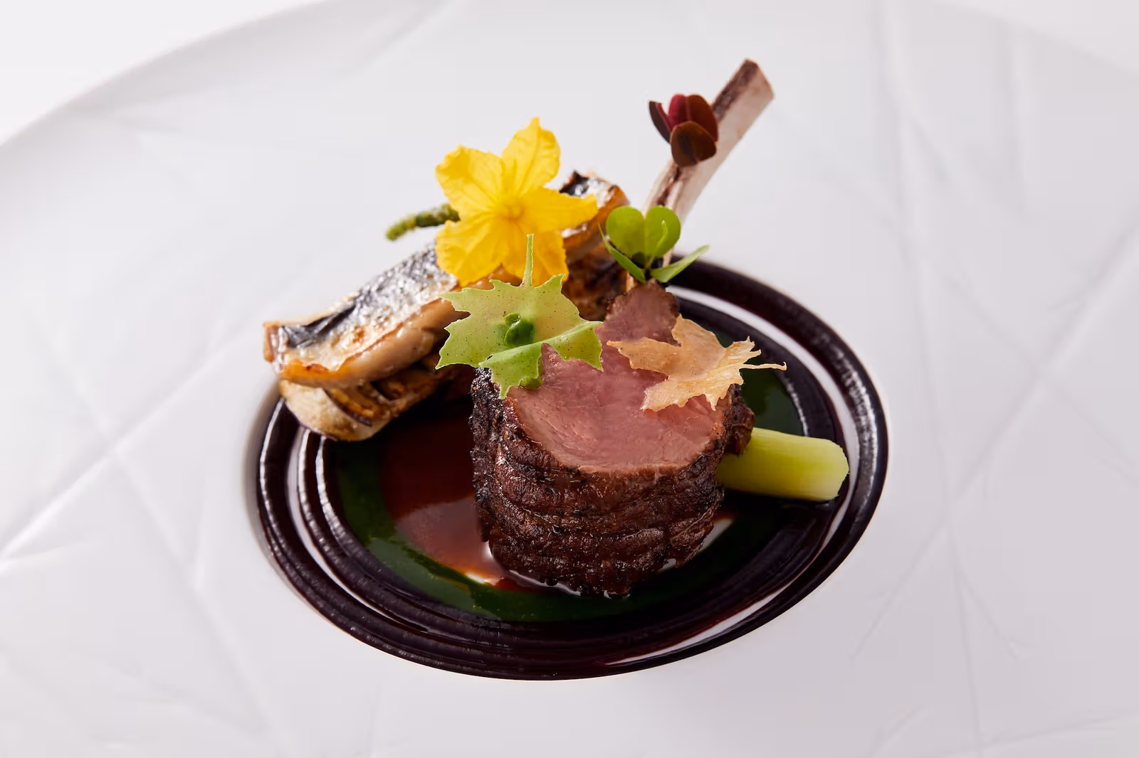 Lamb on dark sauce with leaf-shaped crisps and a yellow flower