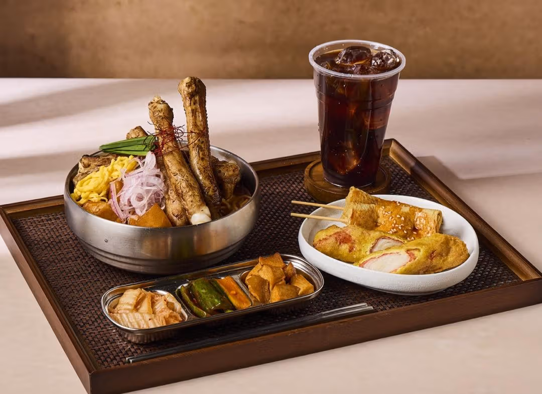 A tray with bone-in meat noodle soup, side dishes, fried items and iced coffee
