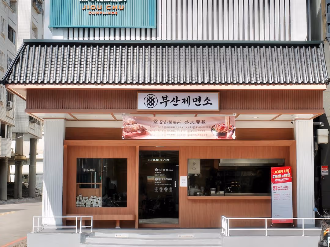 Tiled eaves above Korean noodle-shop lettering and a wood-toned entrance, with JIOU CHU above