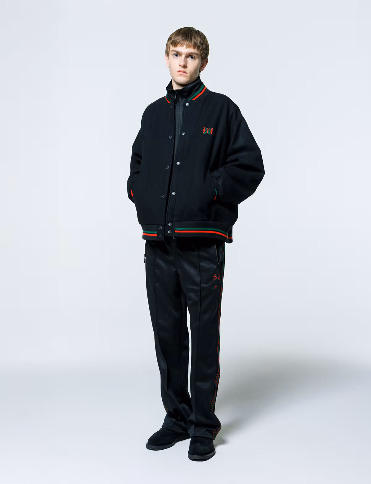 Front view of a model wearing the black NEEDLES ATCQ baseball jacket