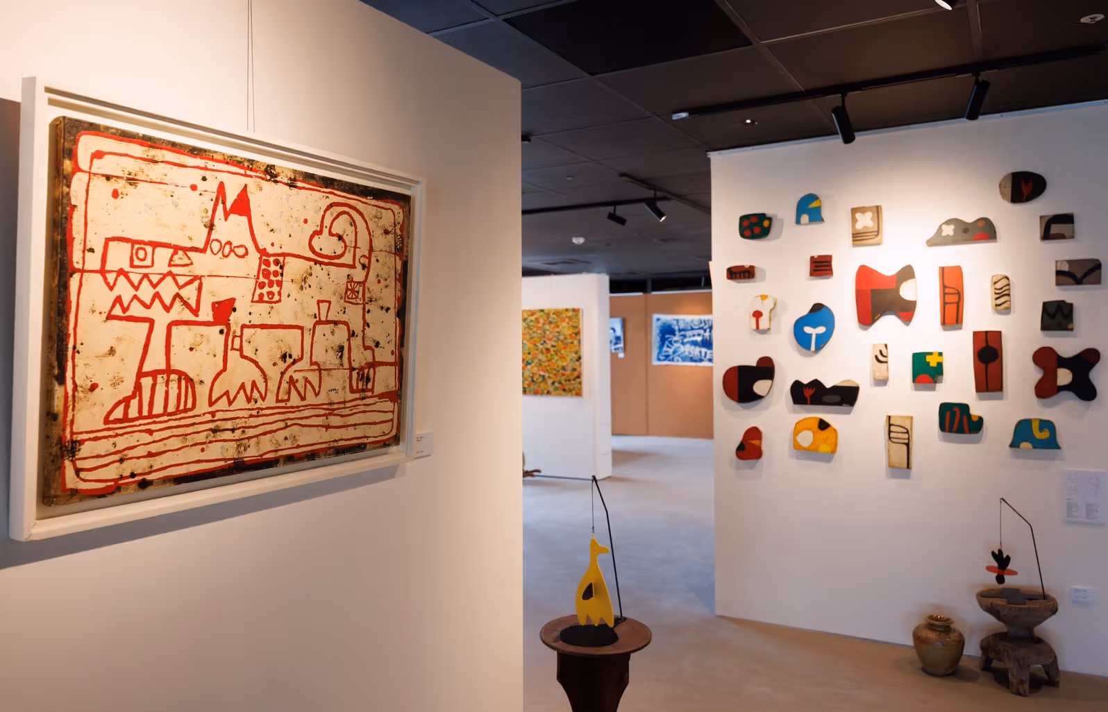 白色展墙上有红线画作、彩色不规则形状，前方有悬吊小件