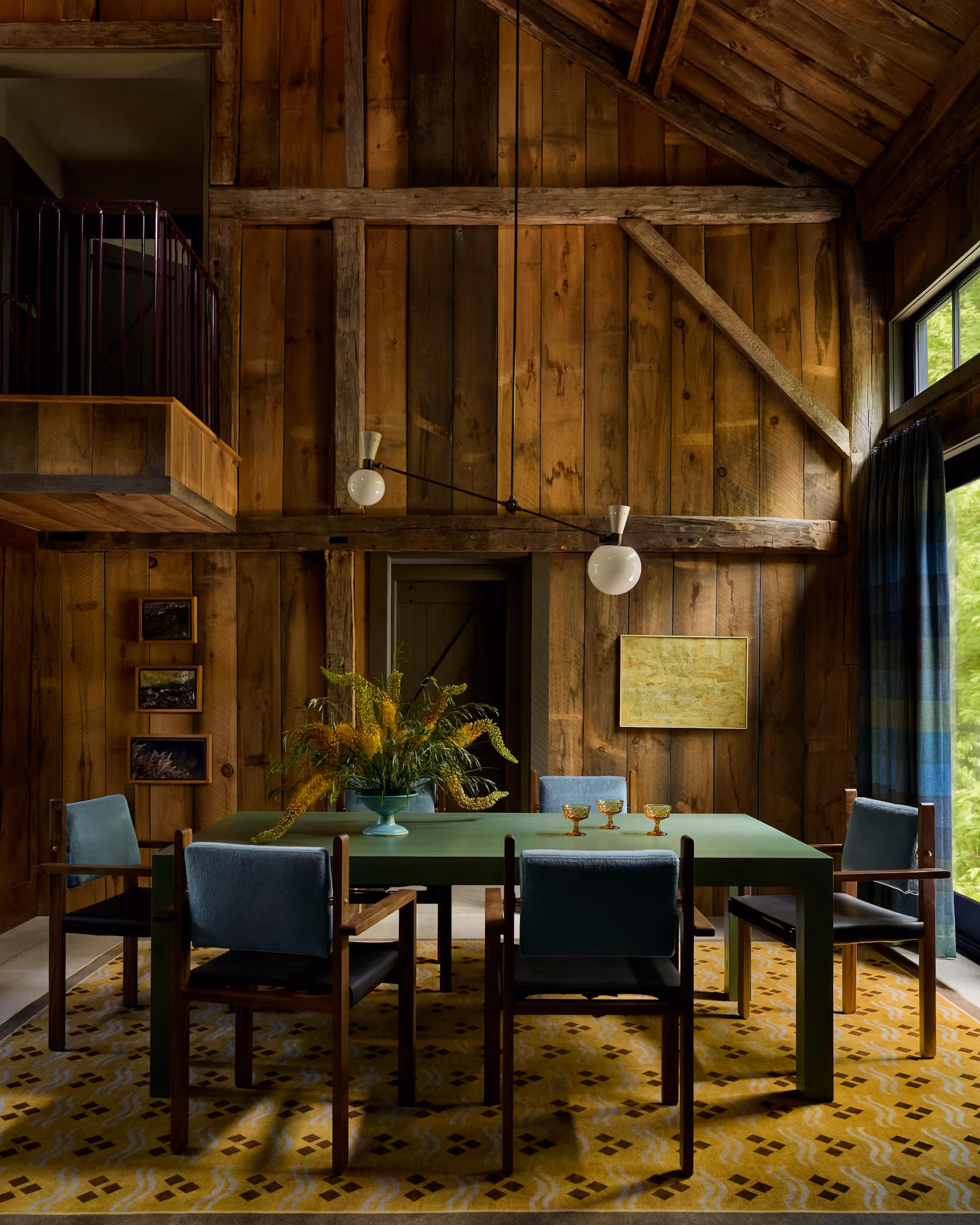 Green dining table and yellow rug in a tall timber room