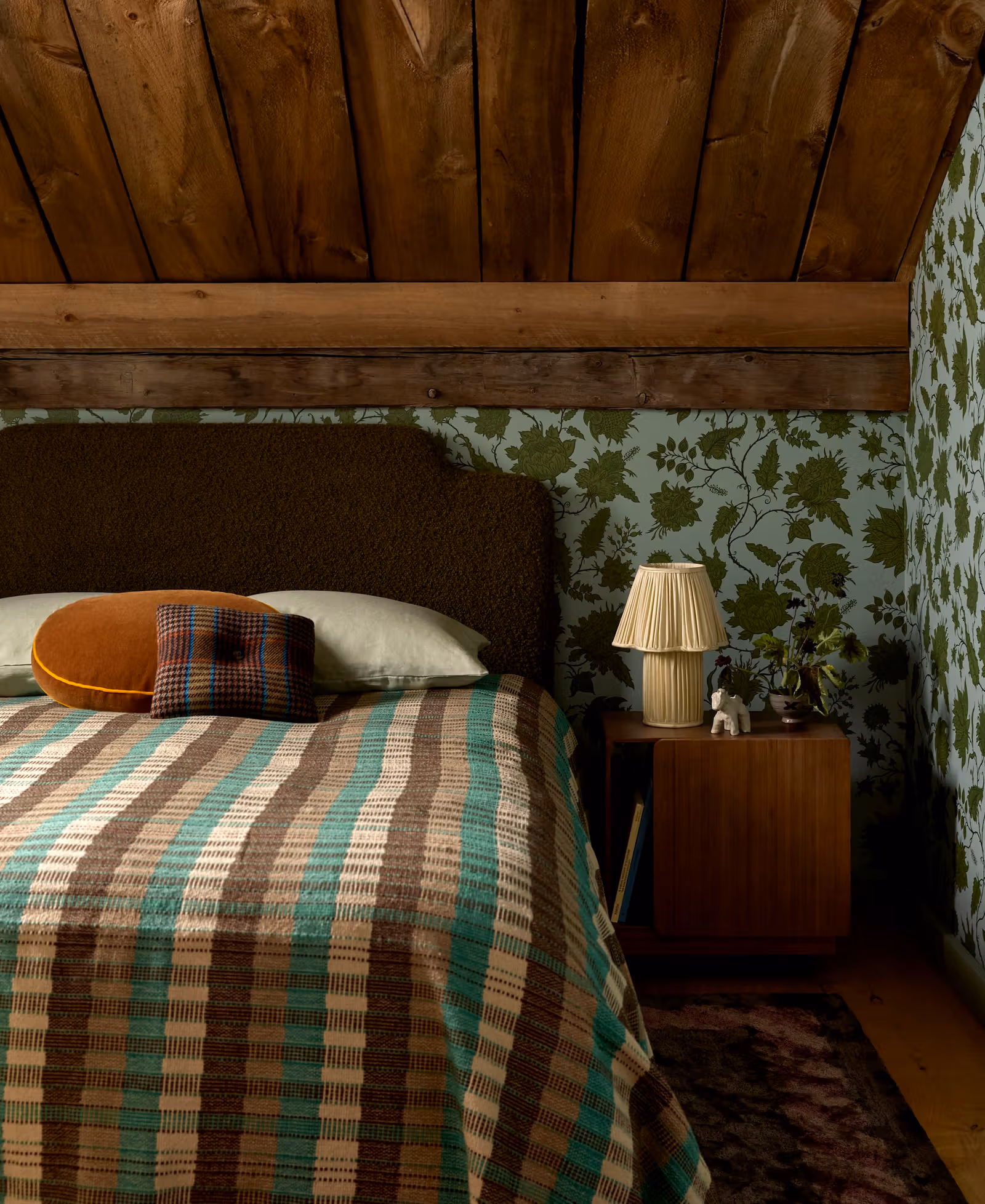 Bedroom with sloping timber roof, striped bedding and botanical wallpaper