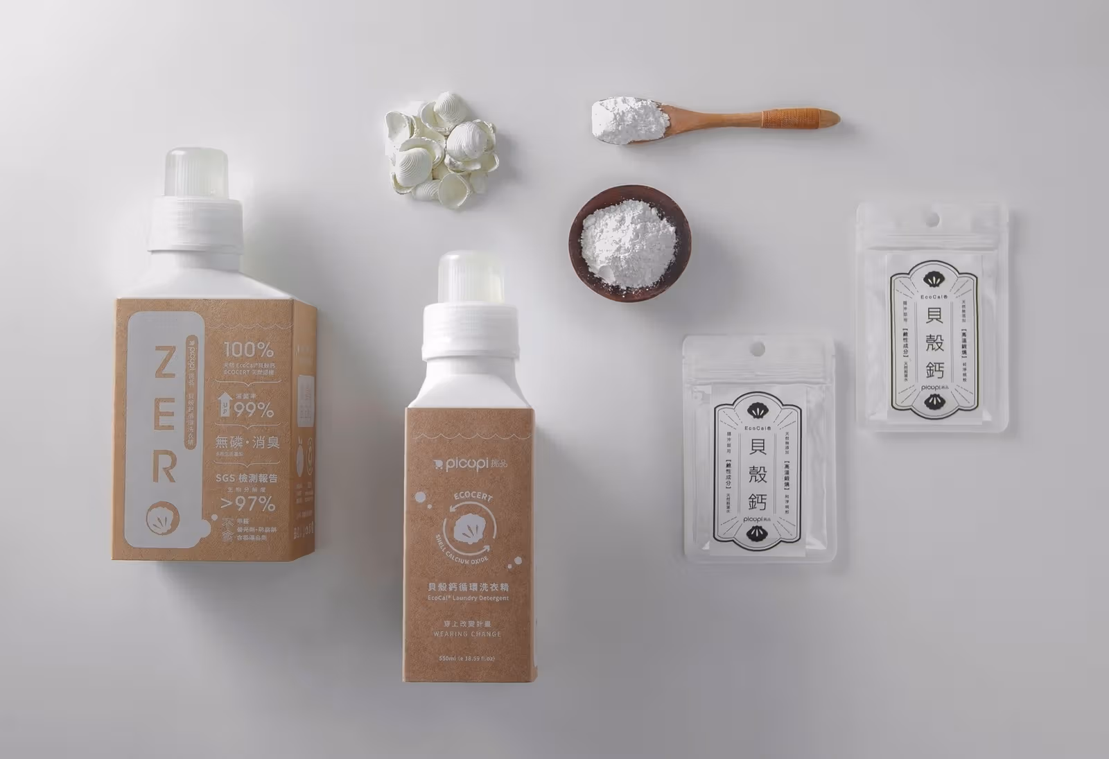 ขวดซักผ้าสีกระดาษคราฟต์ ผงเปลือกหอย และซองแคลเซียมบนพื้นขาว