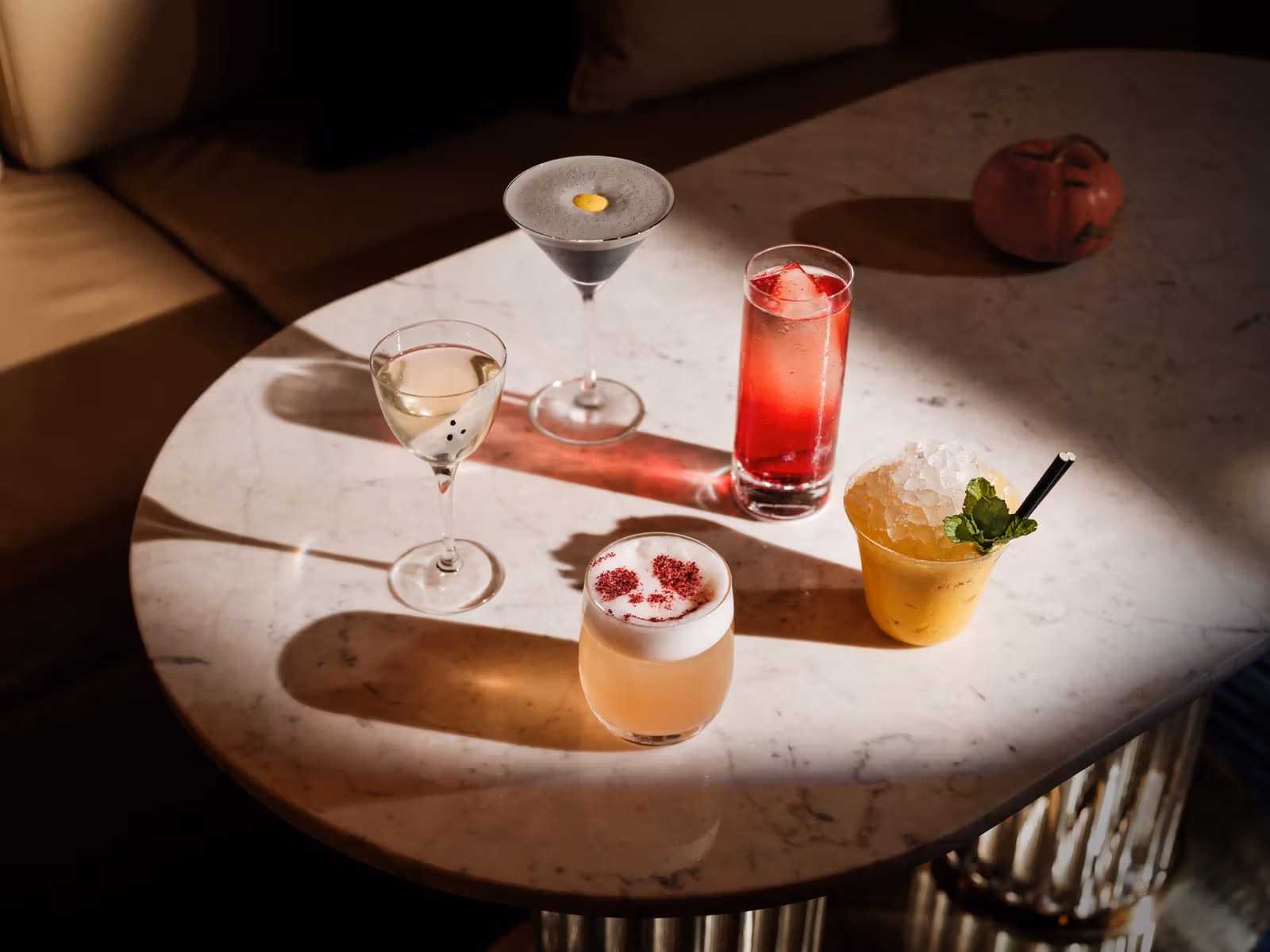 Five cocktails in different colours and glasses on a round stone table