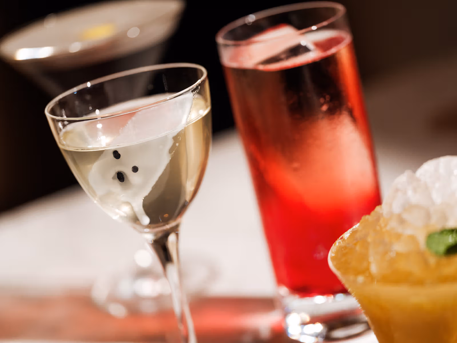 White ghost decoration in a clear stemmed glass beside a tall red drink