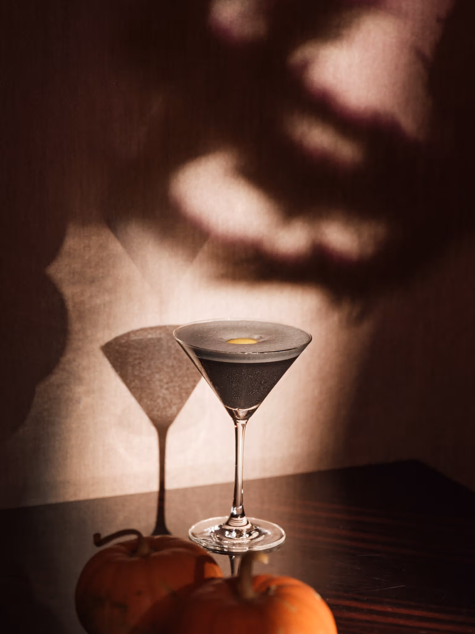 Dark drink in a triangular stemmed glass on wood with a face-like shadow behind