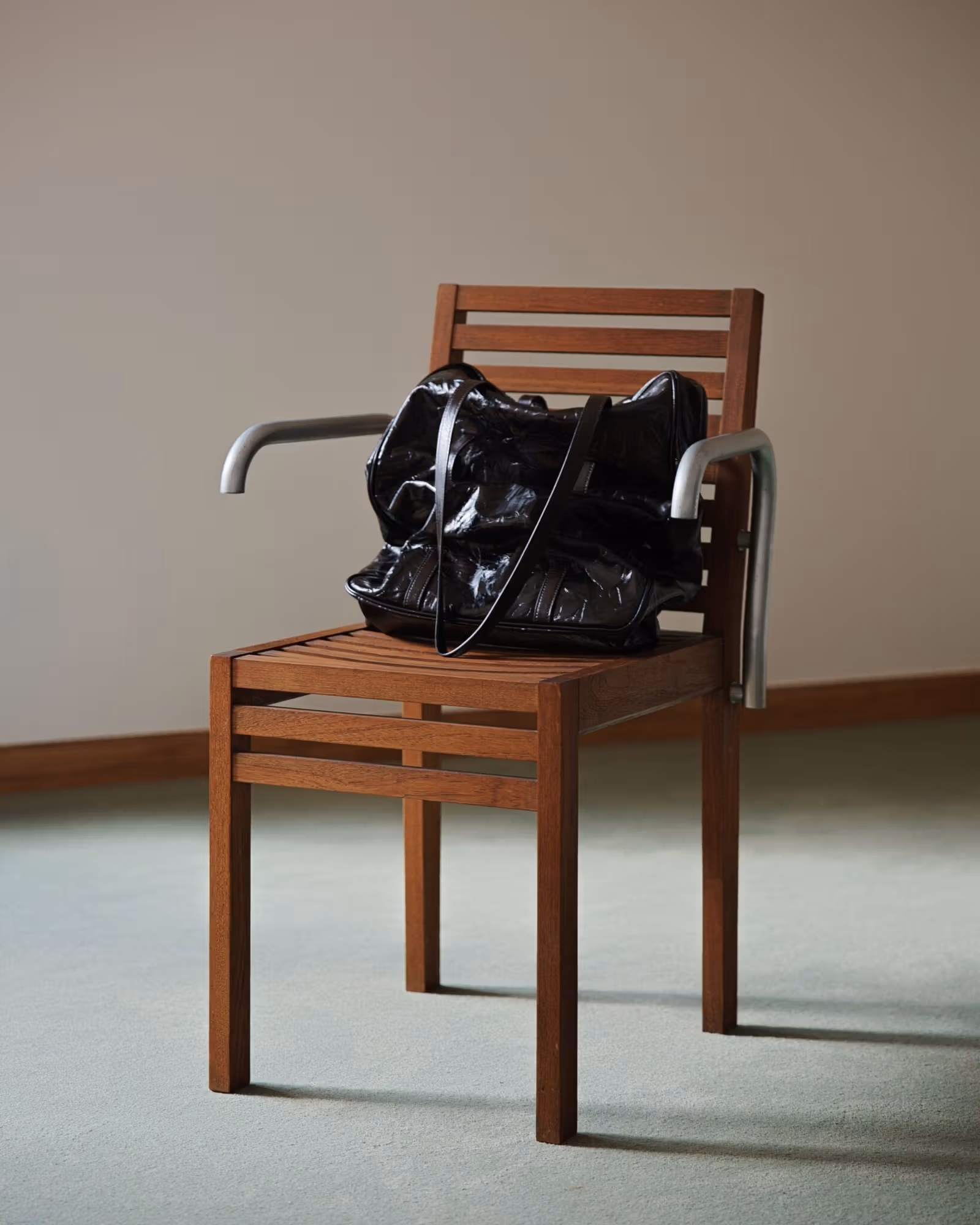 A black handbag on a wooden chair with silver-coloured armrests
