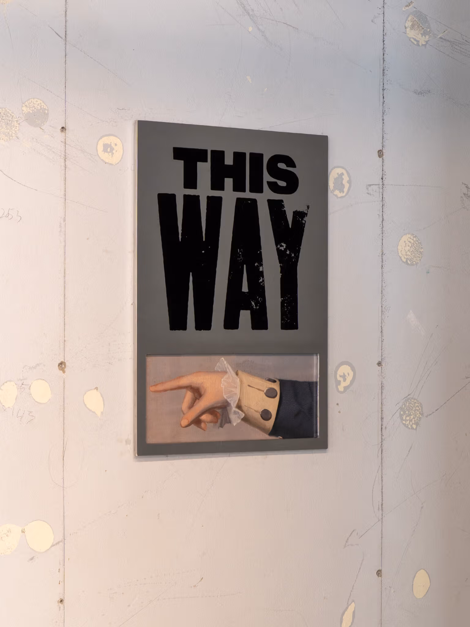 คำสีดำ THIS WAY และภาพมือบุคคลบนผนังอ่อน