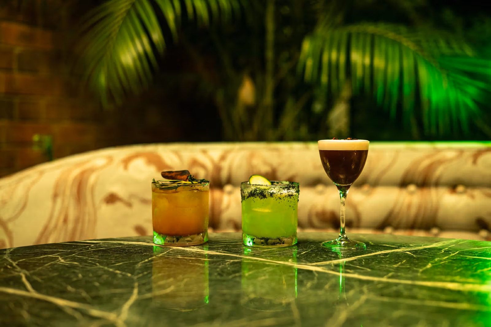 Two green-toned drinks and a dark stemmed drink on a green veined table
