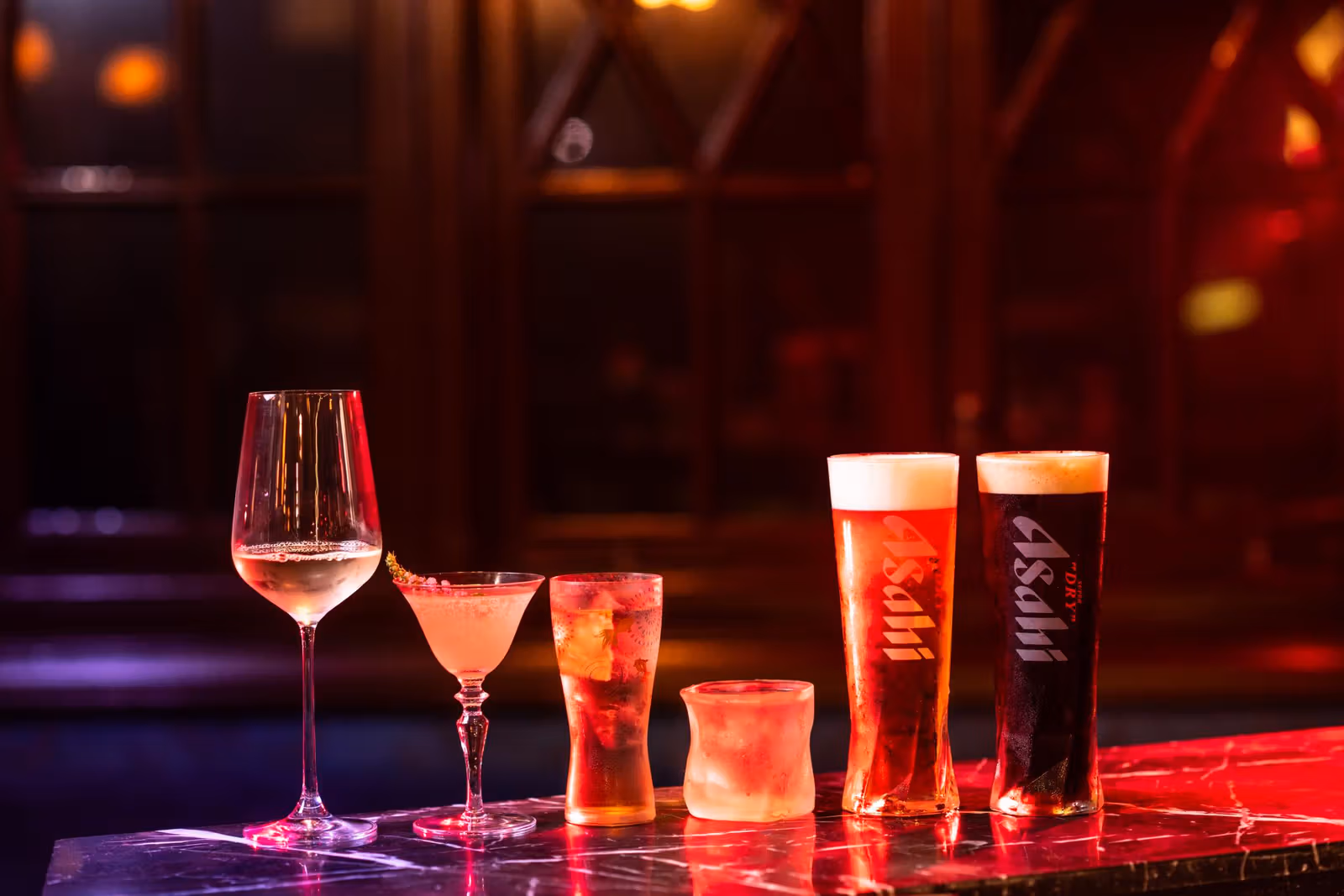 Different glasses and two Asahi-branded beers under red lighting