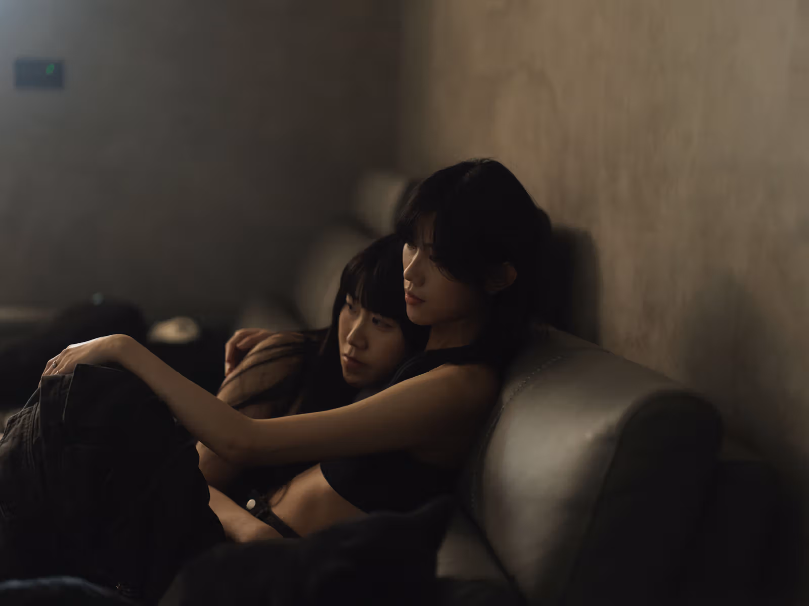 暗い色の服を着た2人がソファに寄り添い、背景に壁と室内の光が見える。
