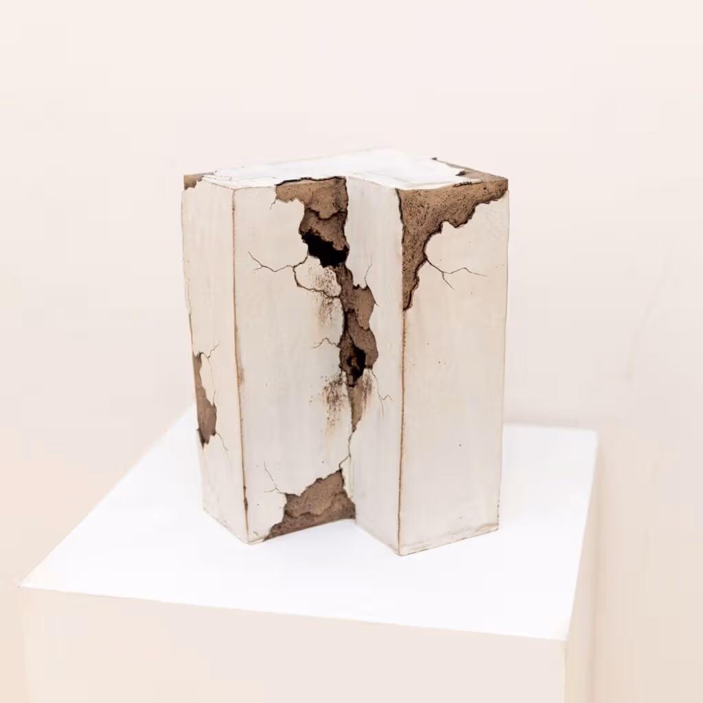 An architectural-corner-like ceramic has pale outer layers, brown peeling areas and fine cracks, displayed on a white plinth.