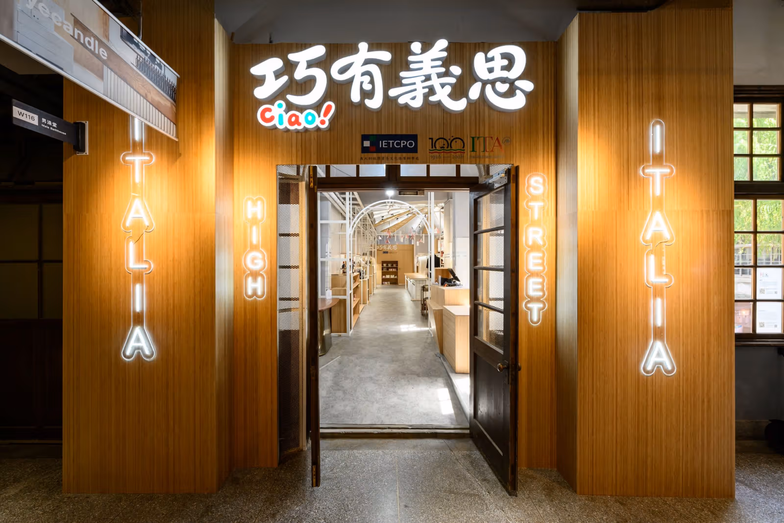 ใต้ป้ายอักษรจีนเรืองแสง มองผ่านประตูเห็นโครงโค้งสีขาวกับดิสเพลย์สีไม้ไผ่