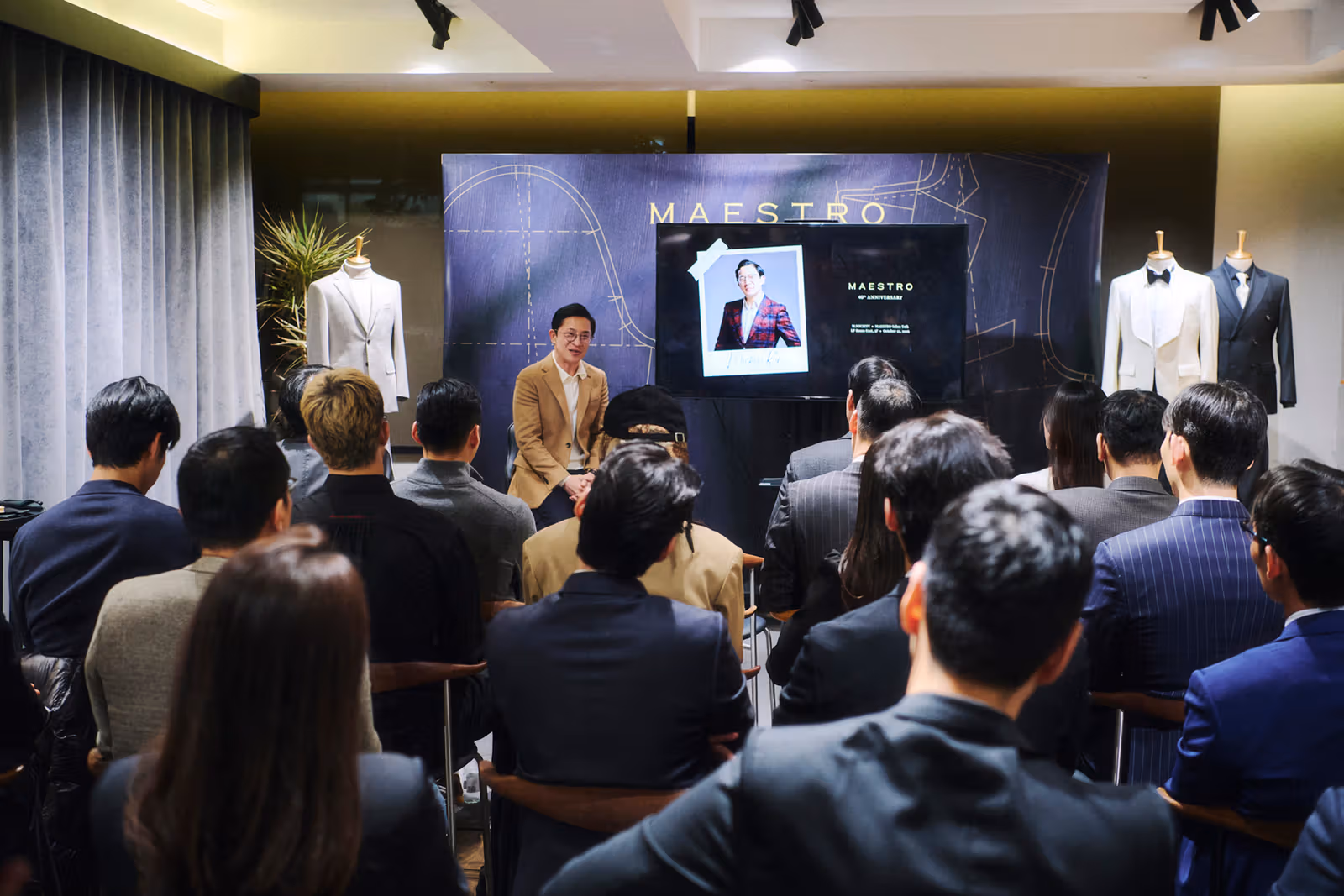 A discussion and suited audience in front of Maestro’s 40th-anniversary backdrop