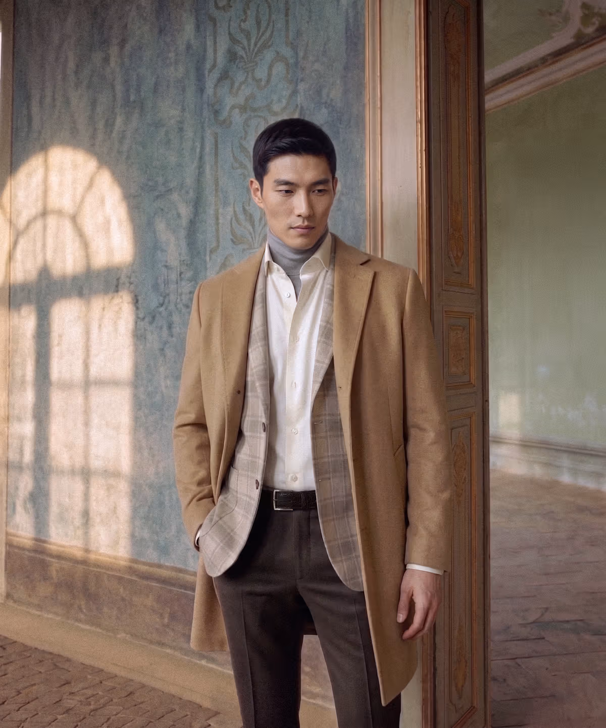 Model in a camel coat, checked jacket and light-colored shirt