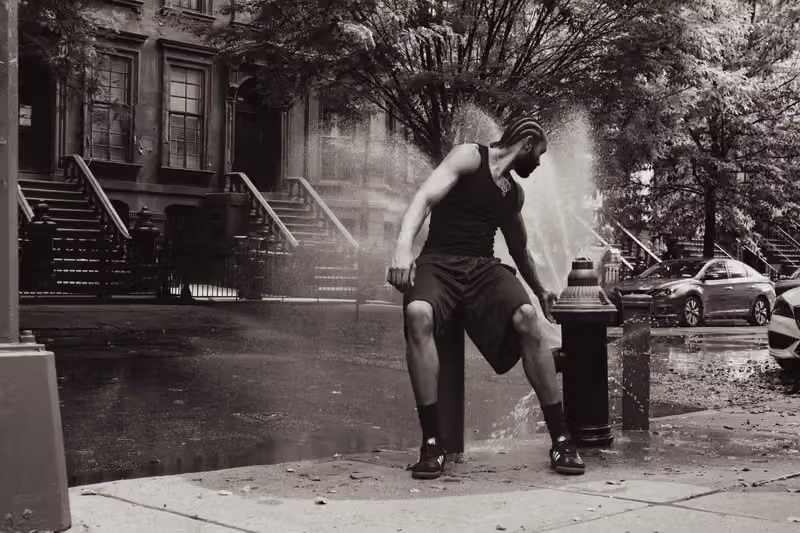 暗いタンクトップとショーツの人物が消火栓と水しぶきのそばに立つ白黒写真