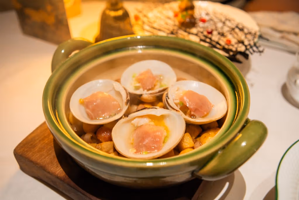 Four open pale shells sit in a green two-handled casserole, each topped with a pink slice.