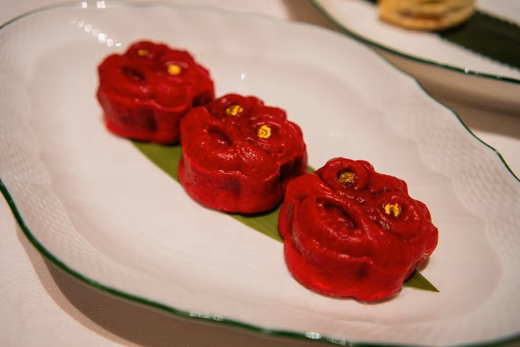 Three red lion-head pastries line a white plate, with small gold-coloured dots at the eyes.