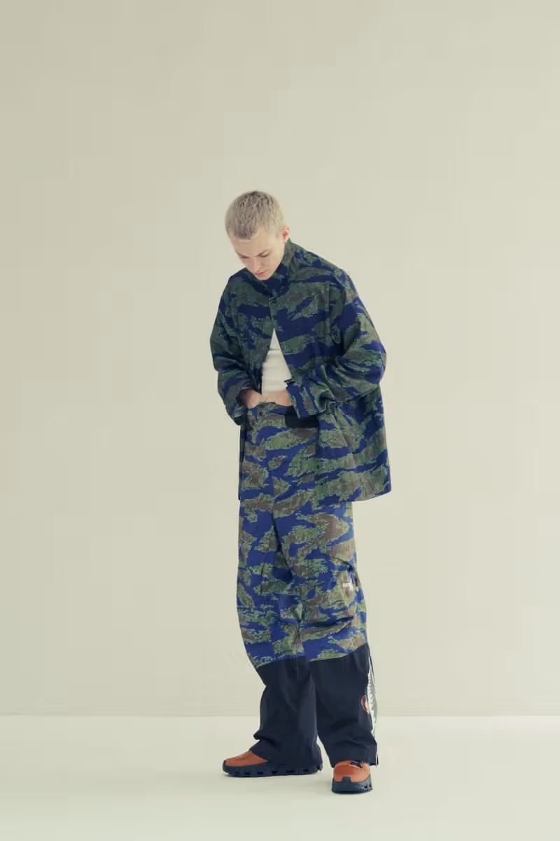 A model in blue-green camouflage outerwear and trousers with brown-black footwear
