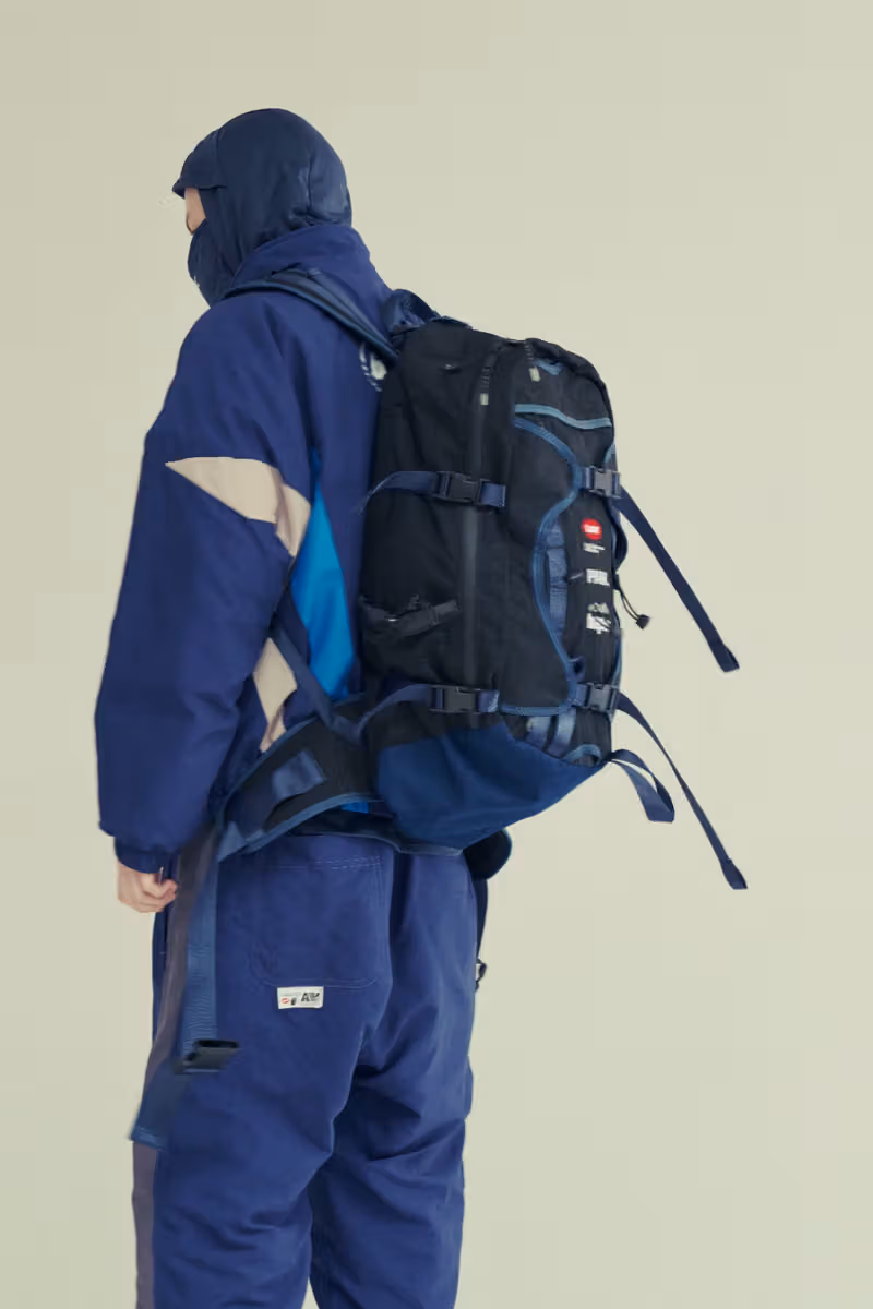 A model in blue clothing carrying a black-and-blue backpack with multiple straps