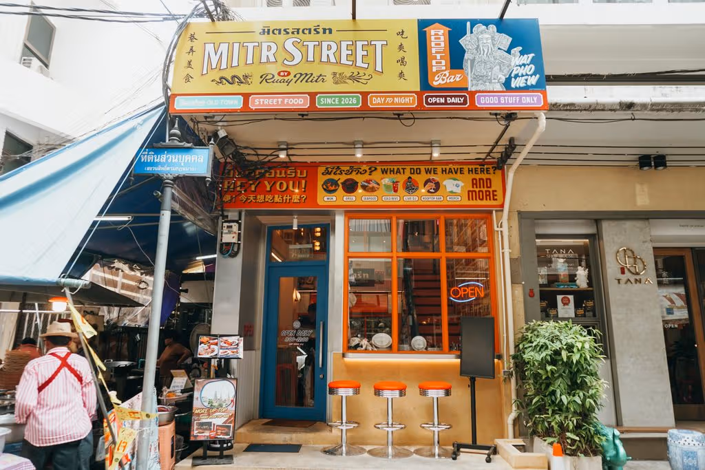 노랑·주황 MITR STREET 간판 아래 파란 문과 붉은 창틀, 빨간 높은 둥근 의자 세 개가 있다.