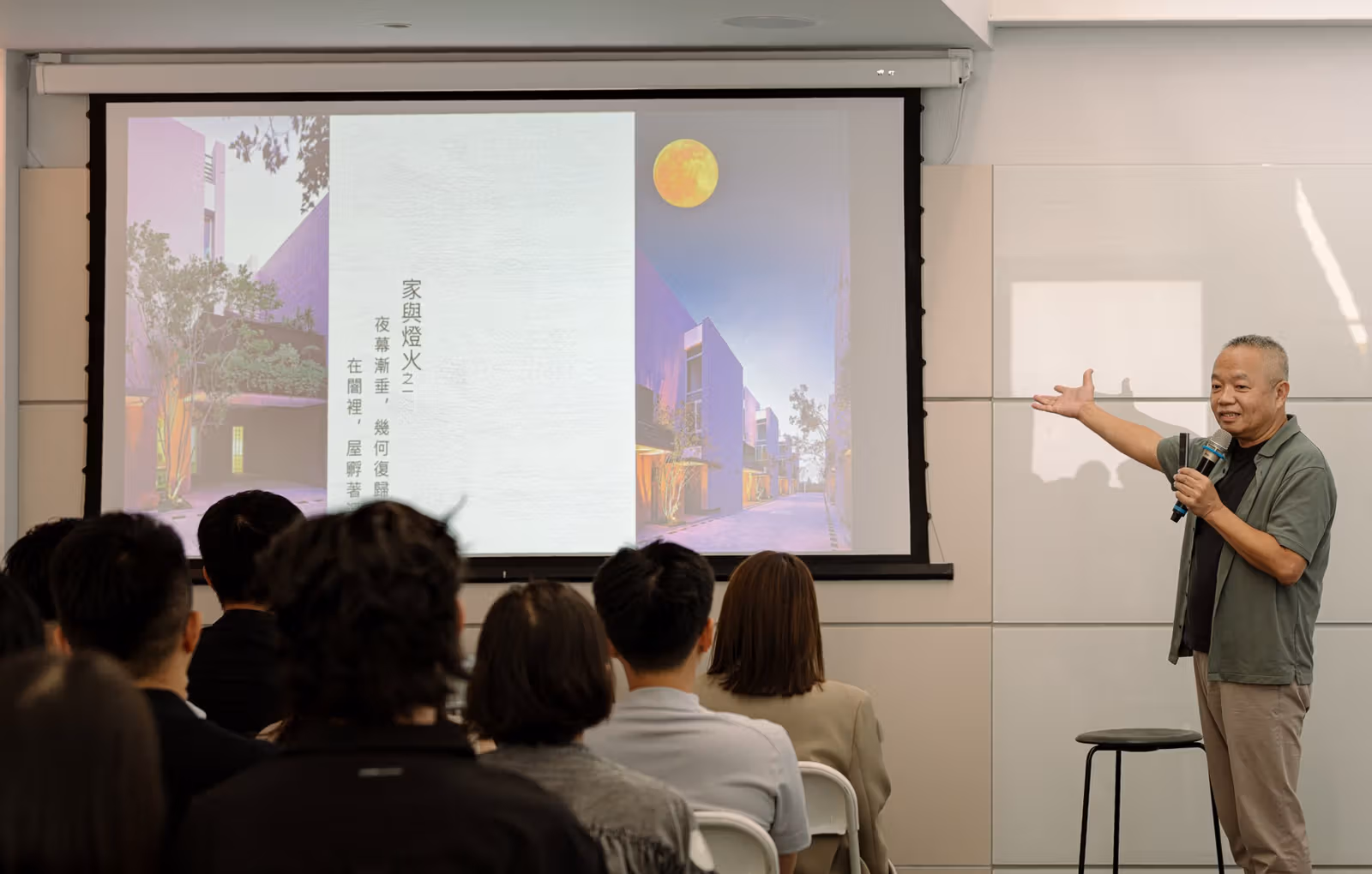 住宅のスライド横でマイクを持ち聴衆に話すウー・ウーイー