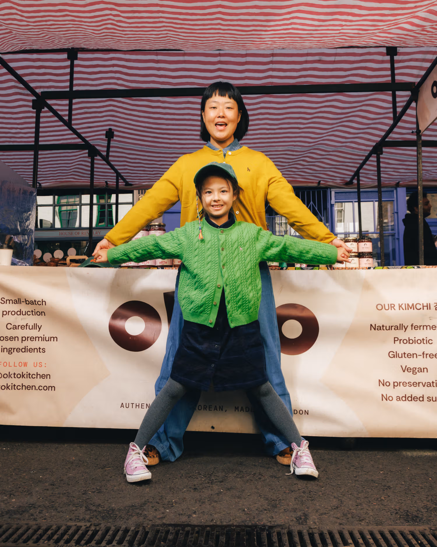 OKTO family members in yellow and green knits extending their arms at the stall