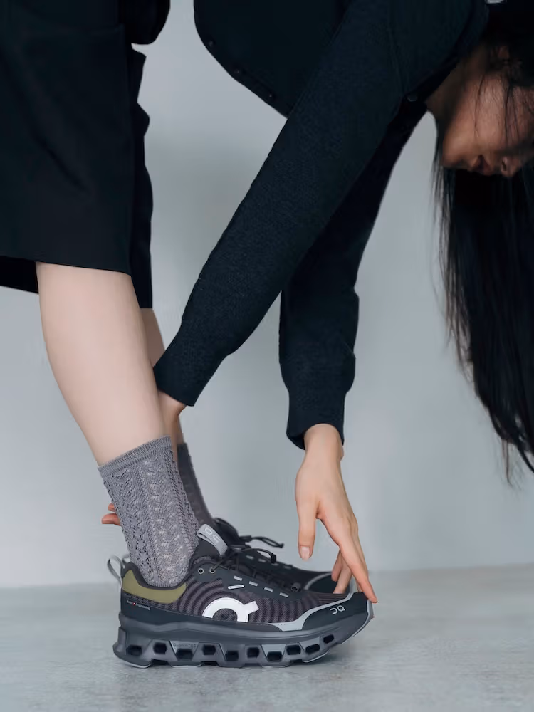 회색 양말과 어두운 옷을 입고 신발 앞코로 손을 뻗는 모델