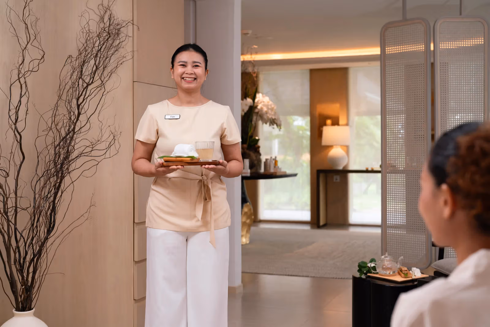 SAii Laguna Phuket 工作人員端著飲品與毛巾，身後為淺色接待空間。
