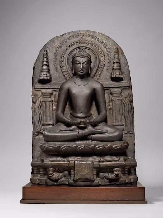 งานหินสีเทายุคปาละ ปลายคริสต์ศตวรรษที่ 10–11 มีพระพุทธรูปนั่ง รัศมี ฐานบัว และองค์ประกอบสองข้าง