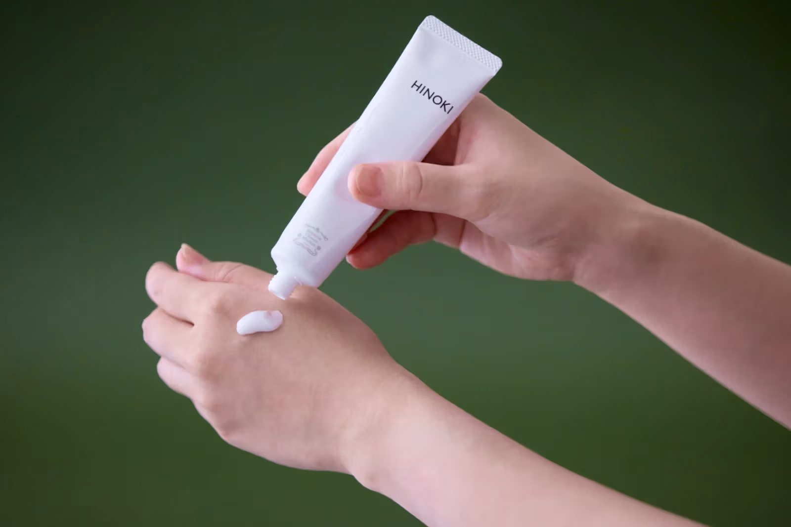 มือบีบครีมสีขาวจากหลอด Hinoki ลงบนหลังมืออีกข้าง