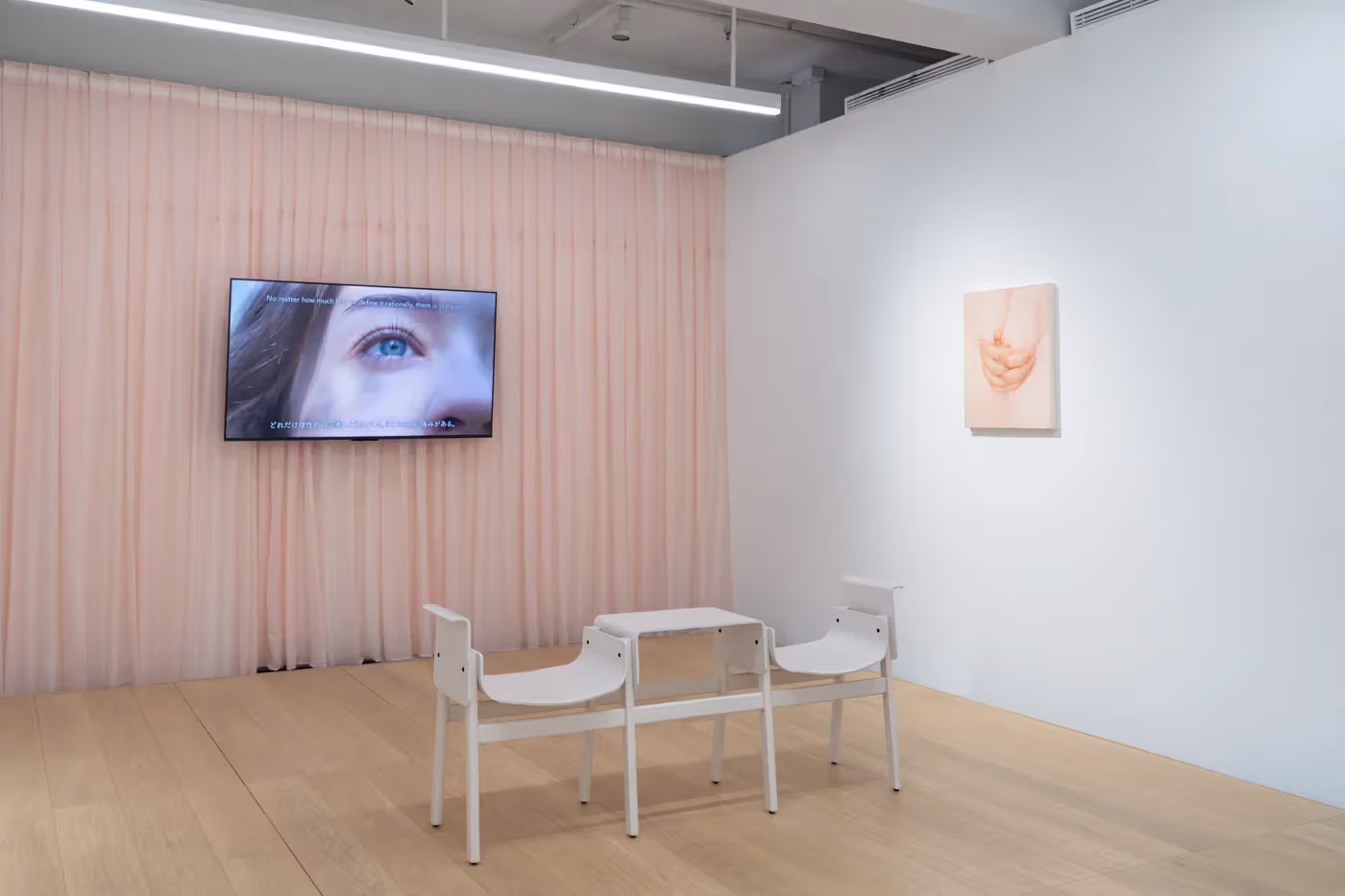 Monitor, curtains and seating form a video viewing area; subtitles belong to the screened work.